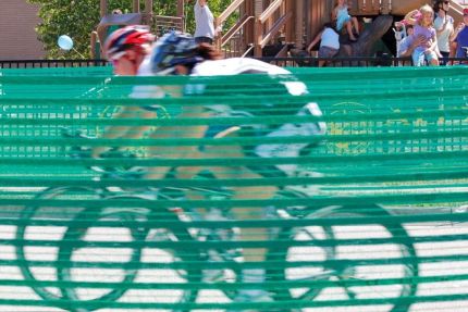 Cyclists on track as seen through green fence